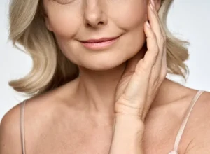 mature woman touching side of face showing midface, chin and neck - centrofacial area that is improved with combined facelift and neck lift surgery. 