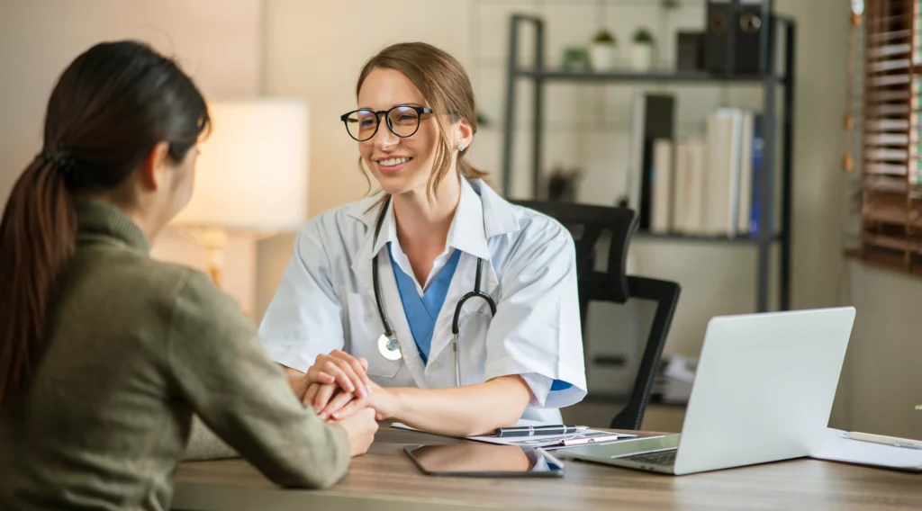 female surgeon in consultation room giving moral support to female patient whilst discussing rhinoplasty procedure