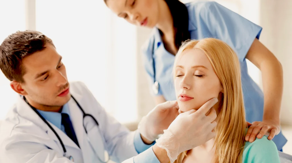 male plastic surgeon assessing female patients chin during patient consultation for genioplasty. Nurse standing in background.