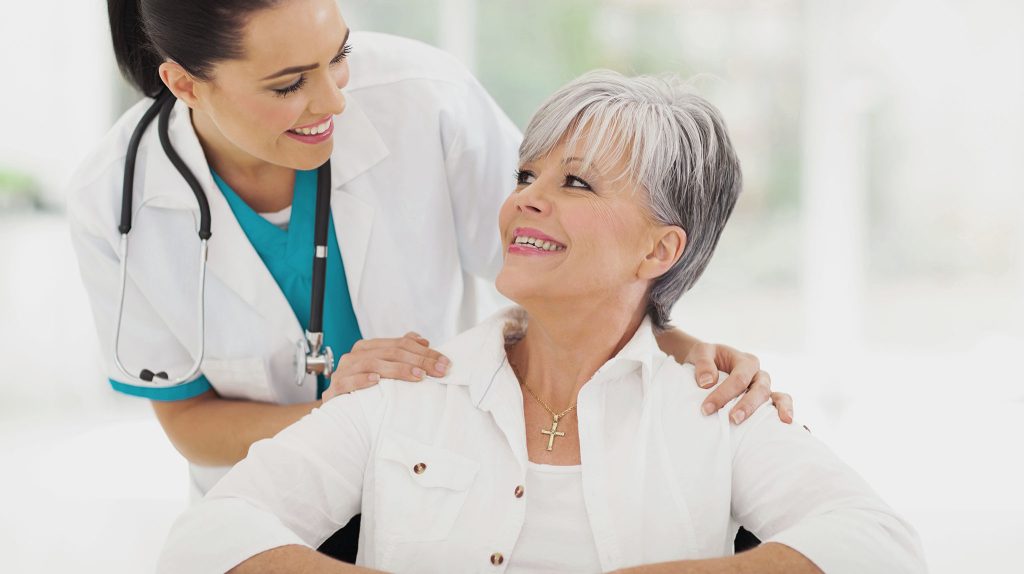 attractive mature woman is seated and smiling up at the female doctor who is standing to her right.